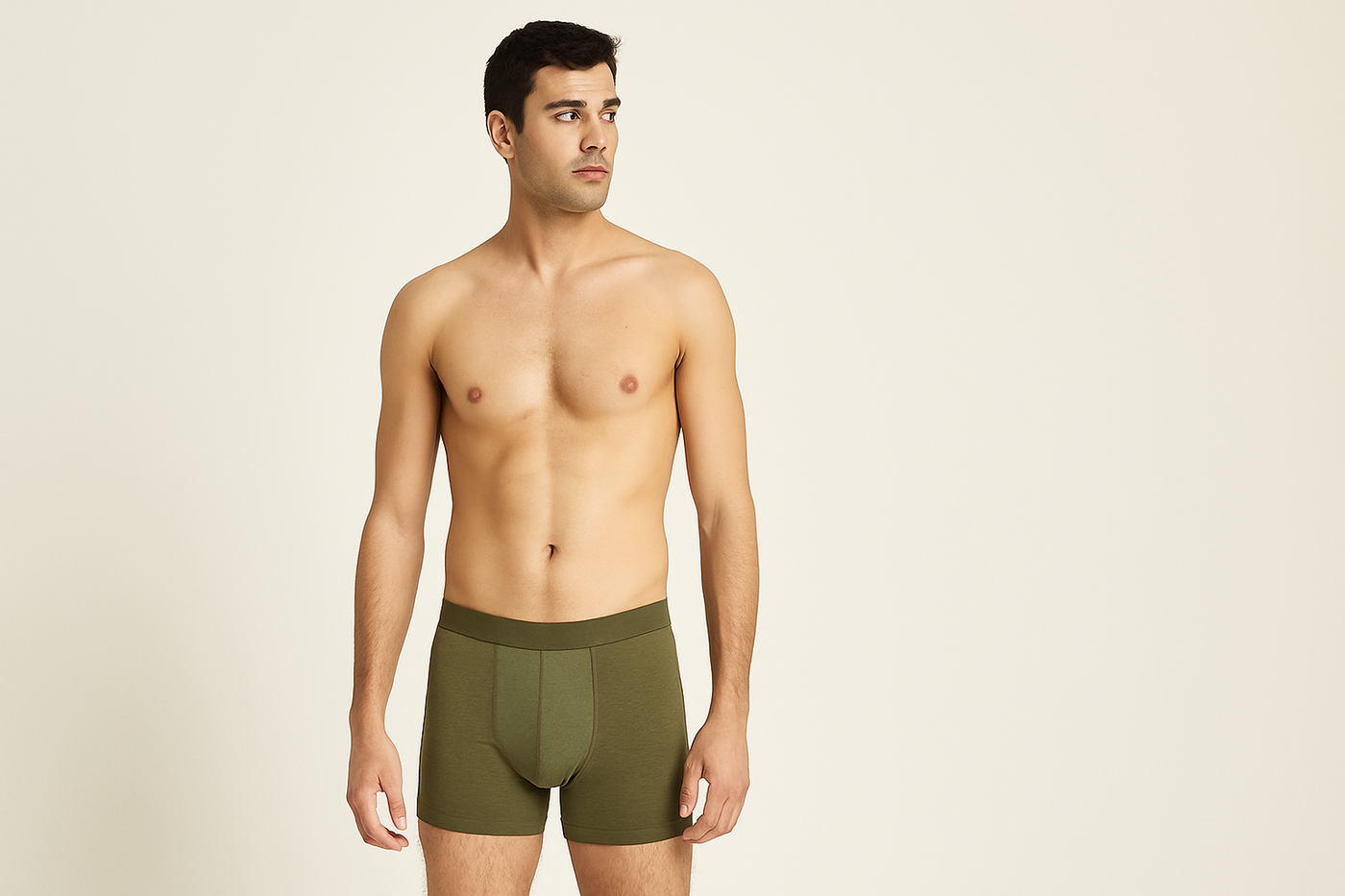 Junger Mann mit olivgrüner Boxershorts aus Bio-Baumwolle steht vor hellem Hintergrund und blickt zur Seite.
